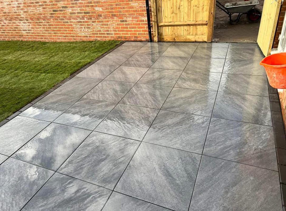 Grey patterned porcelain paving beside a lawn and garden fence
