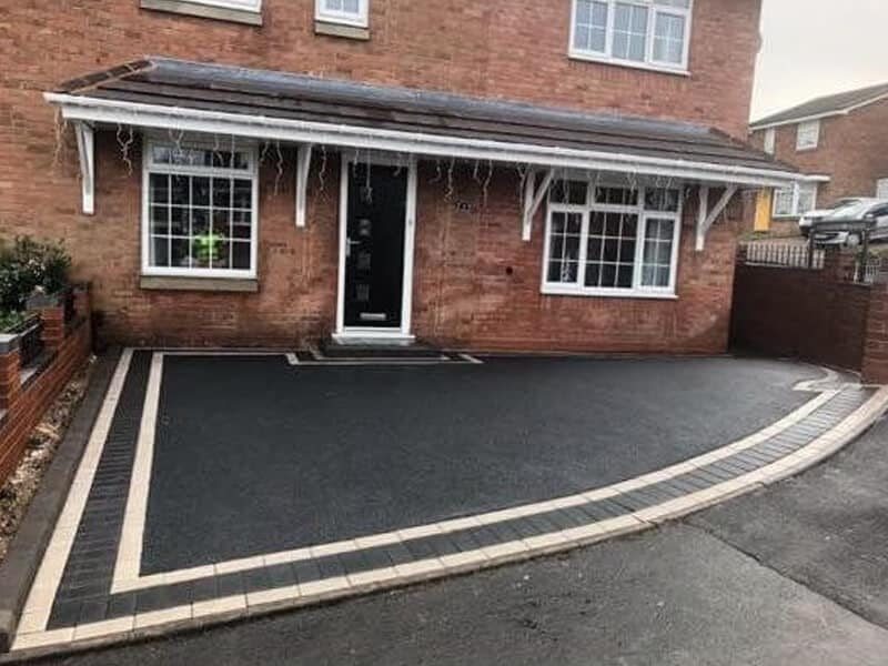 Tarmac driveway with two pale block border lines beside a house